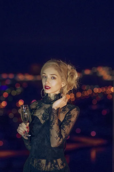 Senhora bonita com copo de champanhe perto da janela com cidade noturna no fundo — Fotografia de Stock