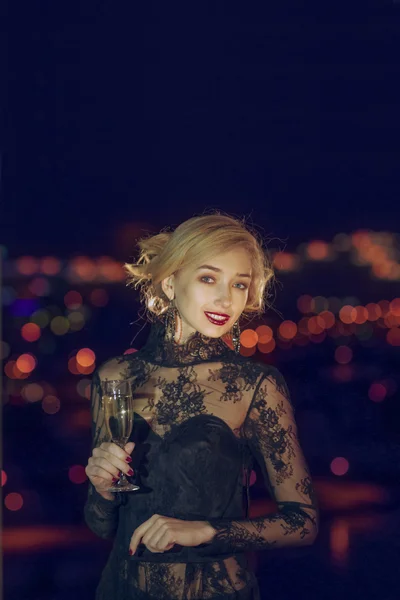Senhora bonita com copo de champanhe perto da janela com cidade noturna no fundo — Fotografia de Stock