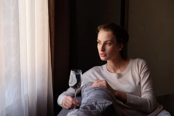 Красива жінка сидить біля вікна в темряві з келихом вина — стокове фото