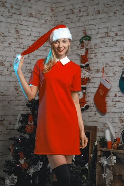 Fille heureuse en robe rouge scolaire et chapeau de Noël posant près de l'arbre de Noël et des cadeaux — Photo