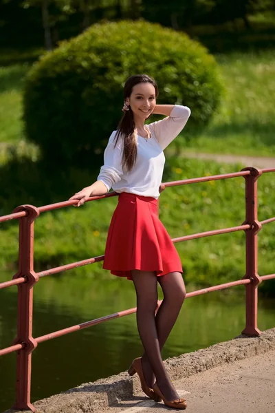 Bella ragazza nel parco in piedi sul ponte sul fiume — Foto Stock