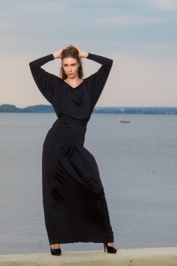 güzel kızla deniz arka plan üzerinde siyah elbiseli bir iskele üzerinde