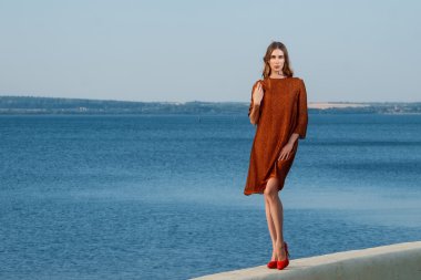 bir iskele ile deniz ve tekneler arka planda Turuncu elbiseli güzel kız