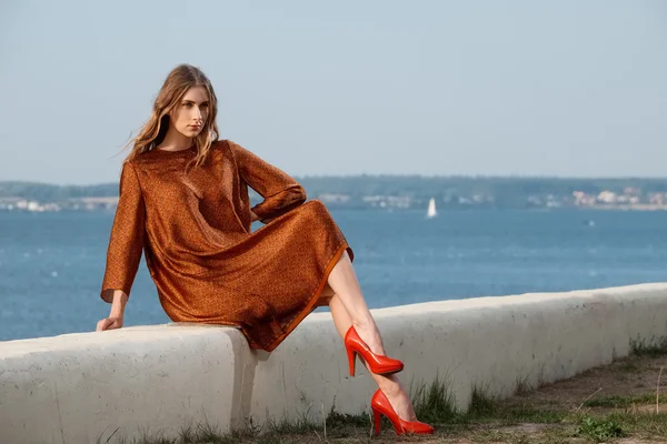 Красивая девушка на пирсе в оранжевом платье с морем и лодки на заднем плане — стоковое фото