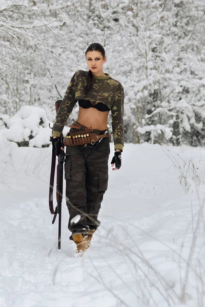 Attraktives Jägermädchen mit Gewehr spazieren im Winterwald — Stockfoto