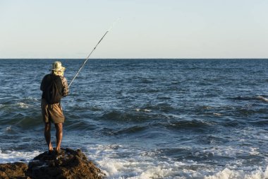 Salvador, Bahia, Brezilya - 25 Nisan 2021: Balıkçı oltasıyla kayalıklarda balık tutuyor. Kızıl Nehir Sahili.