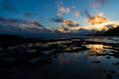 Kumsalın ve kayaların üzerinde mavi ve sarı gün batımı. Salvador, Bahia, Brezilya 'daki Ondina Plajı.
