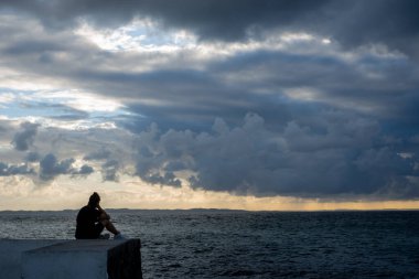 Salvador, Bahia, Brezilya - 09 Mayıs 2021 Ponta do Humait 'te dramatik bir günbatımıyla deniz fenerinin kaya duvarının üstünde yürüyen bir insan.