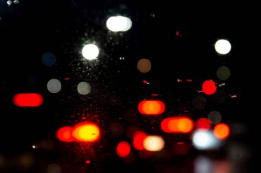 Renkli ışıklar arabanın camından içeri giriyor, yağmur damlalarıyla ıslanıyor. Ağır ve yavaş trafik.