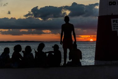 Salvador, Bahia, Brezilya - 23 Mayıs 2021 Ponta do Humait Kalesi 'nin tepesindeki genç insanların silueti turuncu günbatımında.
