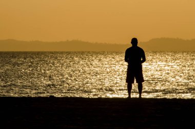 Sarı günbatımında bir insanın silueti. Ribeira Plajı, Salvador, Bahia, Brezilya.
