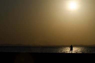 Sarı günbatımında bir insanın silueti. Ribeira Plajı, Salvador, Bahia, Brezilya.