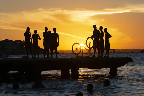 Salvador, Bahia, Brazil - March 09 2019: Silhouette of young people jumping from the Crush bridge at the yellow sunset on Ribeira beach in Salvador (BA).