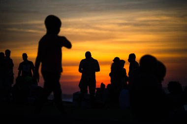 Salvador, Bahia, Brezilya - 12 Haziran 2021: Salvador, Bahia 'da Farol da Barra' nın muhteşem renkli günbatımının tadını çıkaran insanların silueti.
