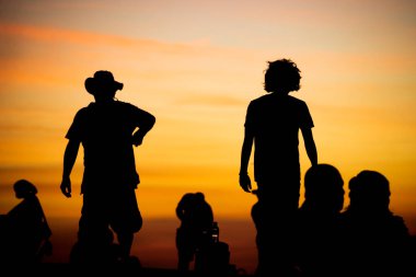 Salvador, Bahia, Brezilya - 12 Haziran 2021: Salvador, Bahia 'da Farol da Barra' nın muhteşem renkli günbatımının tadını çıkaran insanların silueti.