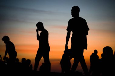 Salvador, Bahia, Brezilya - 12 Haziran 2021: Salvador, Bahia 'da Farol da Barra' nın muhteşem renkli günbatımının tadını çıkaran insanların silueti.