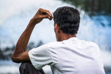 Çimenlerde tek başına oturan adam Dique do Tororo 'ya bakıyor, düşünüyor. Salvador, Bahia, Brezilya.