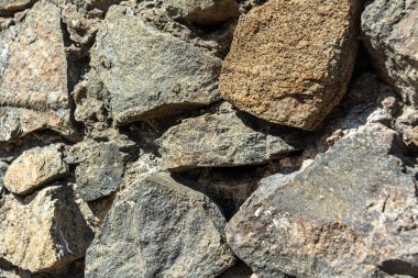 Düzensiz taşlarla örülmüş ve havan topuyla birleştirilmiş bir duvarın fotoğrafı. Görüntü kayaların pürüzlü dokularını ve doğal ışık altındaki toprak tonlarını vurgular..