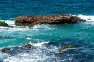 Sahildeki kayaların arasında hareket eden deniz manzarası. Görüntü bir huzur ve doğanın gücünü aktarıyor..