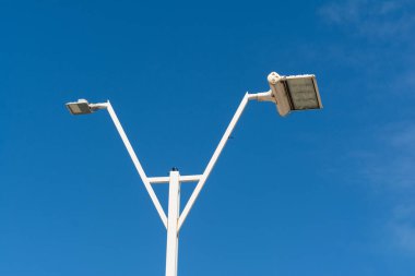 Mavi gökyüzüne karşı spot ışıkları olan bir sokak lambası. Yayalar için gece aydınlatması.