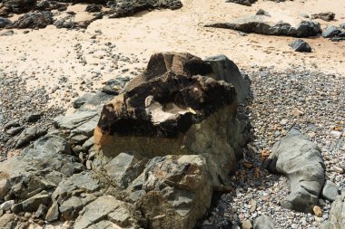 Kaya oluşumları ve deniz kenarındaki doğal havuzlarla panoramik bir sahil manzarası. Mavi okyanus, parçalı bulutlu bir gökyüzünün altında ufka doğru uzanıyor ve tropikal kıyıların tipik sakin ve doğal atmosferini oluşturuyor..