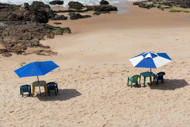 Yukarıdan çekilen bir görüntü, açık ve güneşli kumsalda terk edilmiş bir sahili gösteriyor. Önemli olan, asil mavi ve beyaz çizgili şemsiye.