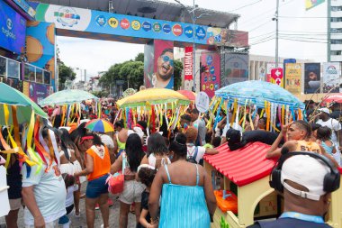 Salvador, Bahia, Brezilya - 14 Şubat 2026: Bahia 'daki Salvador Karnavalı' nın arka planında yaşayan insanlar ve yeşil şemsiyeli bir şemsiyenin altında asılı duran birkaç renkli kurdelenin görüntüsü.