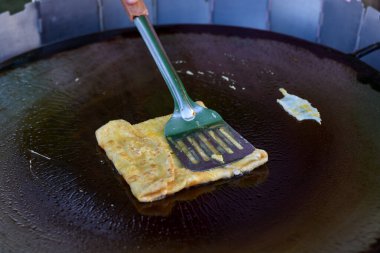 Sıcak bir ızgarada yumurta krepi pişirilir, spatula ve maşayla katlanır..