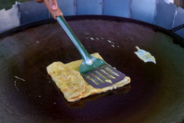 Sıcak bir ızgarada yumurta krepi pişirilir, spatula ve maşayla katlanır..