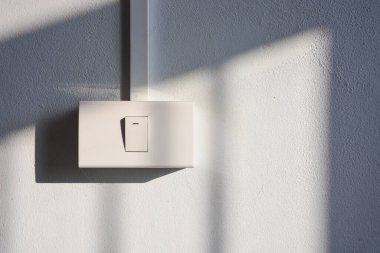 Kalıplı beyaz bir duvarda güçlü gölgeleri olan ışık düğmesi..