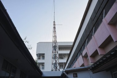 Açık gökyüzüne karşı binalar arasında iletişim kulesi yükseliyor.