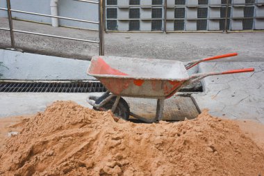 Beton yüzeydeki kum yığınının yanındaki el arabası.