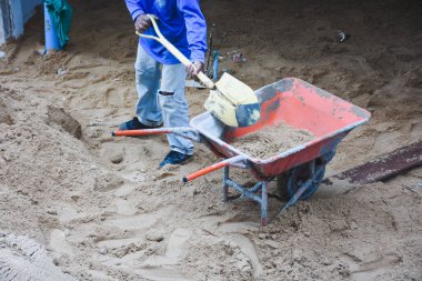 Beton yüzeydeki kum yığınının yanındaki el arabası.