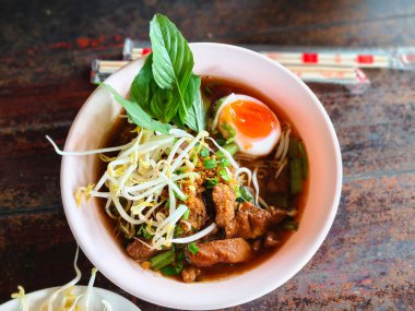 İçinde taze et dilimleri, pirinç eriştesi, fasulye filizi, yeşil soğan, çıtır sarımsak, fesleğen ve yağda kaynamış yağda pişirilmiş yağda yumurta bulunan Tayland usulü şehriye çorbası..