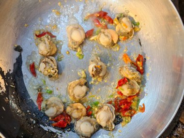 Sıcak tavada kızartılmış taze deniz tarakları ve sarımsak, cızırdayan yağ, zengin doku ve yakın çekim pişirme sahnesinde canlı malzemeler..