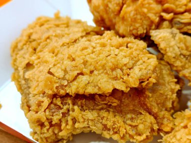 Beyaz karton kutuda servis edilen çıtır çıtır kızarmış tavuk parçaları. Sıcak hafif fast food tarzında makro çekimde sulu et görünür..