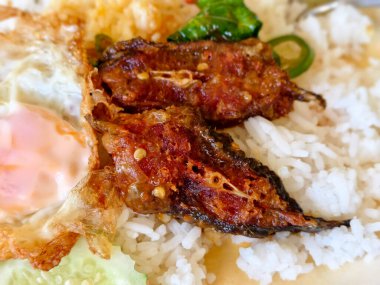 Otantik Tayland pedi ped pla duk tod baharatlı kırmızı köri soslu kızarmış yayın balığı parçaları ve fesleğen. Kızarmış yumurta ve taze salatalık dilimli pilav.