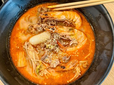 Karides, sığır eti, pirinç keki ve baharatlı kırmızı bir çorbaya serpiştirilmiş mantar, zengin dokular ve lezzet içeren susam tohumları.