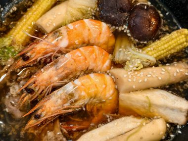 Sebzeler, mantarlar ve susam tohumlarıyla kaynayan karidesin üst görüntüsü, zengin dokular ve taze malzemeler gösteriyor.