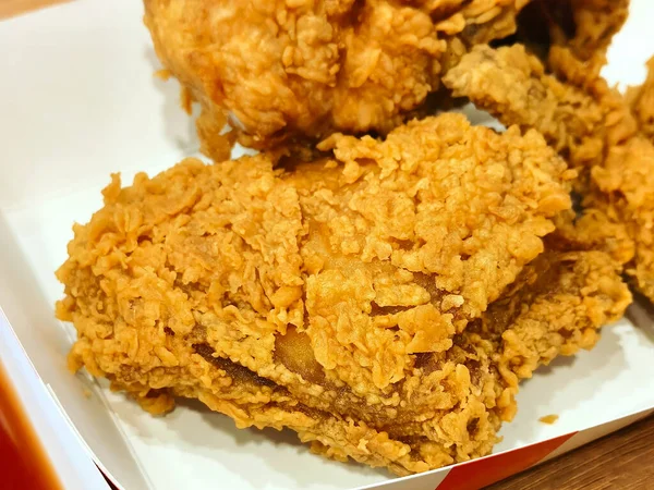Kırmızı süslemeli beyaz paket servis kutusunda çıtır çıtır kızarmış tavuk parçaları. Sulu et, sıcak ışık altında makro fast food tarzında gizlice bakar..