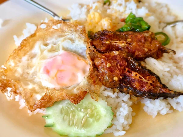 Otantik Thai pad ped pla duk tod baharatlı kırmızı köri soslu ve fesleğenli kızarmış yayın balığı içerir. Kızarmış yumurta, salatalık ve yeşil biberli pilav ile servis edilir..