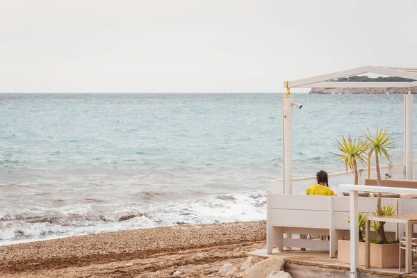 scenic view of woman sitting in a restaurant and watching the sea. Rear view of a woman at the restaurant front the sea