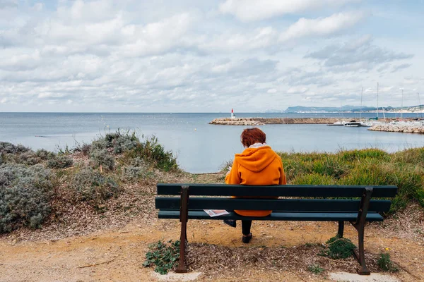 Deniz kenarındaki bir bankta dinlenen bir kadının arka görüntüsü.