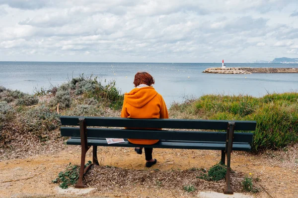 Deniz kenarındaki bir bankta dinlenen bir kadının arka görüntüsü.
