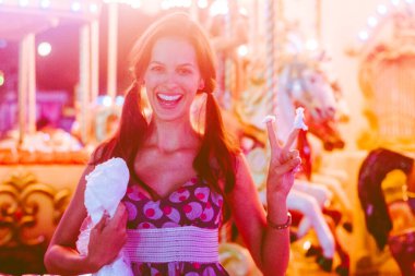 Atlıkarınca 'nın önünde fotoğraf, pamuk şeker, elbiseli kız, sarı ışık, gülümseyen yüz, parmaklar, iki numara, huzur..