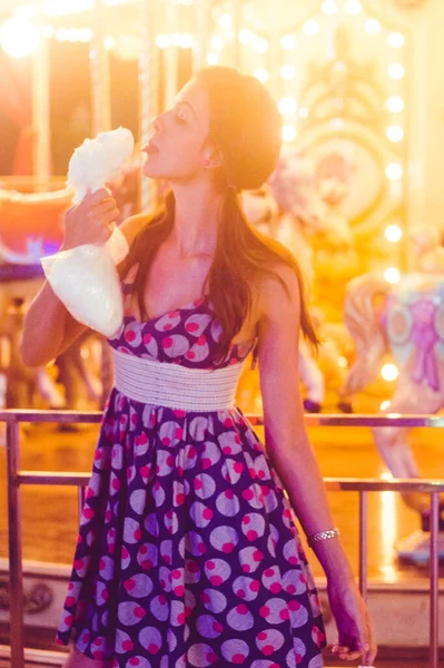 Atlıkarıncanın önünde fotoğraf, pamuk helva yemek, dil, elbise giymiş kız, sarı ışık.