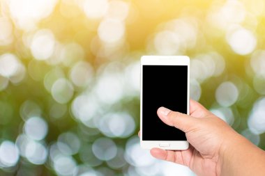 adam elini tutun ve dokunmatik ekran akıllı telefon üzerinde gün öğlen ışık yeşil bulanık doğa arka plan ile.