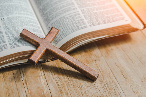 the cross over opened bible on wood table with window light.