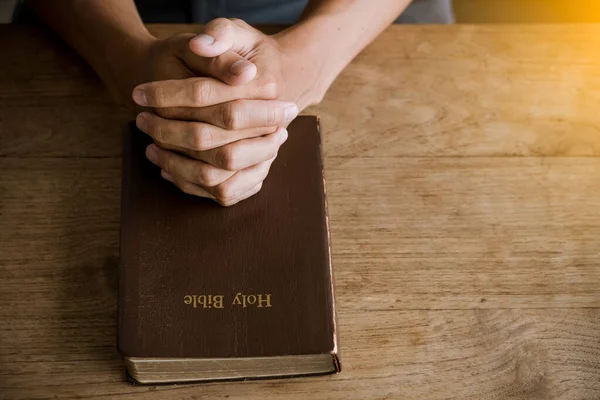 Prayer hands over a Holy Bible on wood table with window light.concept to faith.christian backgound