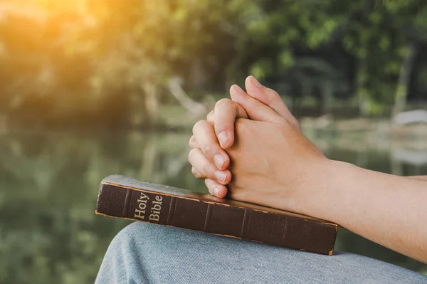 Woman praying on nature background.Hands folded in prayer on a Holy Bible for faith, spirituality and religion